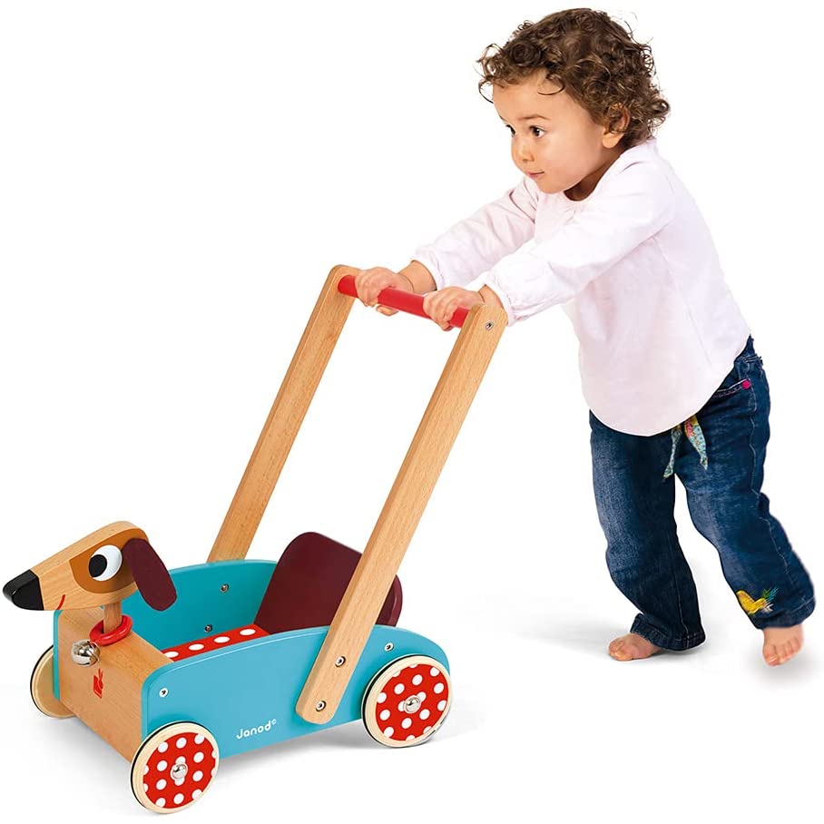Enfant pieds nus penché en avant poussant un chariot de marche en bois bleu à roues rouges
